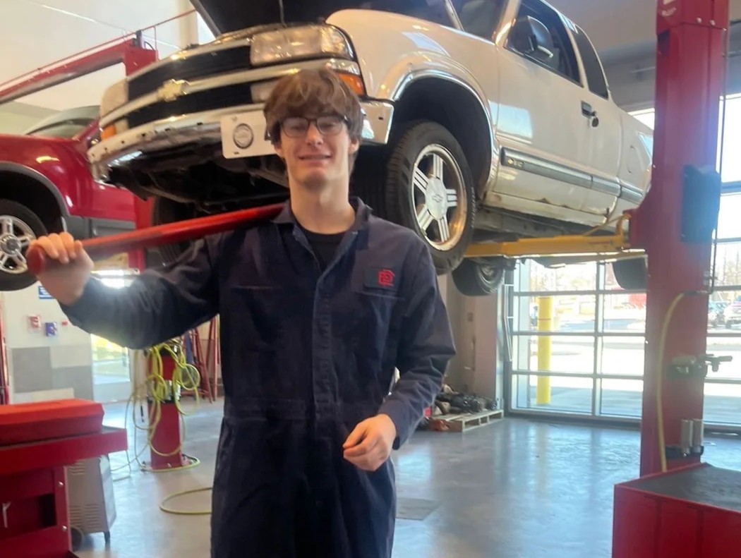 Jacob Poore in an automotive workshop beside a truck on a lift